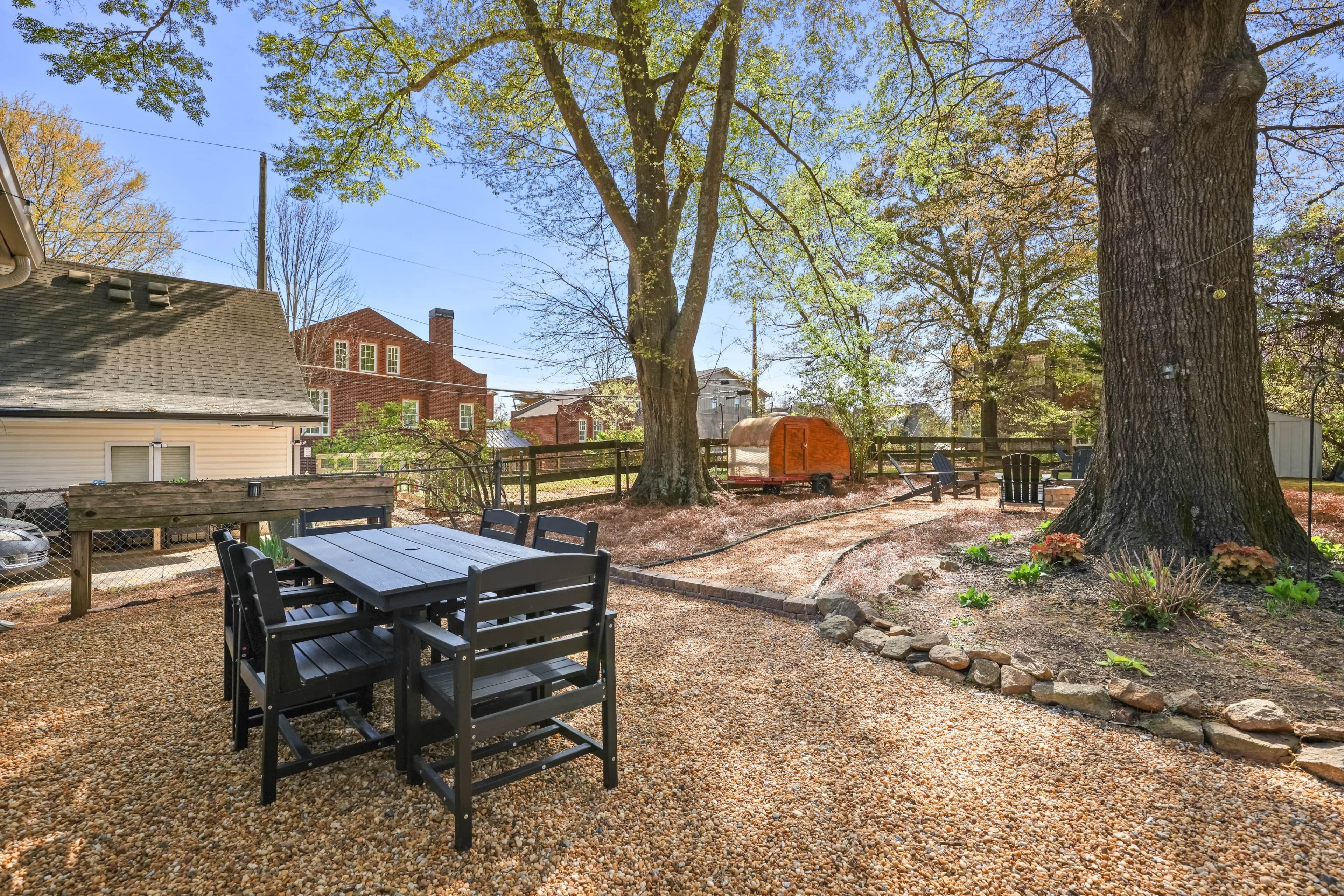 Un espace extérieur aménagé en terrasse, avec une table et des chaises, entouré de gravier et d’arbres.