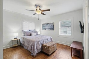A bedroom with a bed, a ceiling fan, a bedside table with a lamp, a wall-mounted TV, and a window with blinds. - Walk to Marietta Square|Renovated 3BR|Fenced Yard (Marietta)