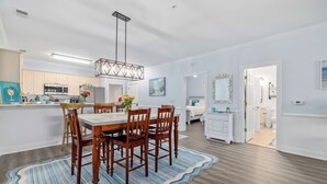 Una cocina moderna con armarios blancos, una isla central y un comedor con mesa y sillas de madera.