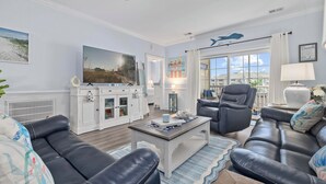 Una sala de estar con un televisor grande, sofás de cuero, una mesa de centro y vista al mar por la ventana.