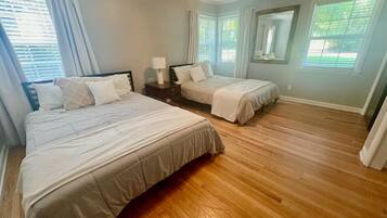 Une chambre avec deux lits, une table de chevet, un miroir et de grandes fenêtres équipées de stores.