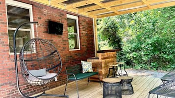 Une terrasse couverte avec un fauteuil suspendu, un banc et une petite table.