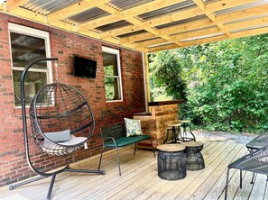 Une terrasse couverte avec un fauteuil suspendu, un banc et une petite table.