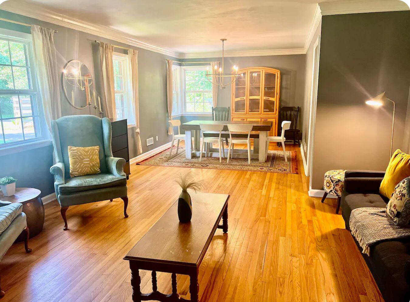 Un salon avec un plancher en bois, un coin repas avec une table et des chaises, un fauteuil bleu, un canapé et un meuble.