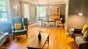 Un salon avec un plancher en bois, un coin repas avec une table et des chaises, un fauteuil bleu, un canapé et un meuble.