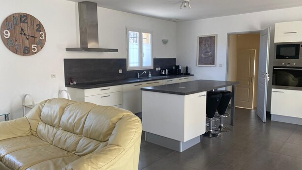 Een moderne keuken met een centraal eiland, een bank en een klok aan de muur.