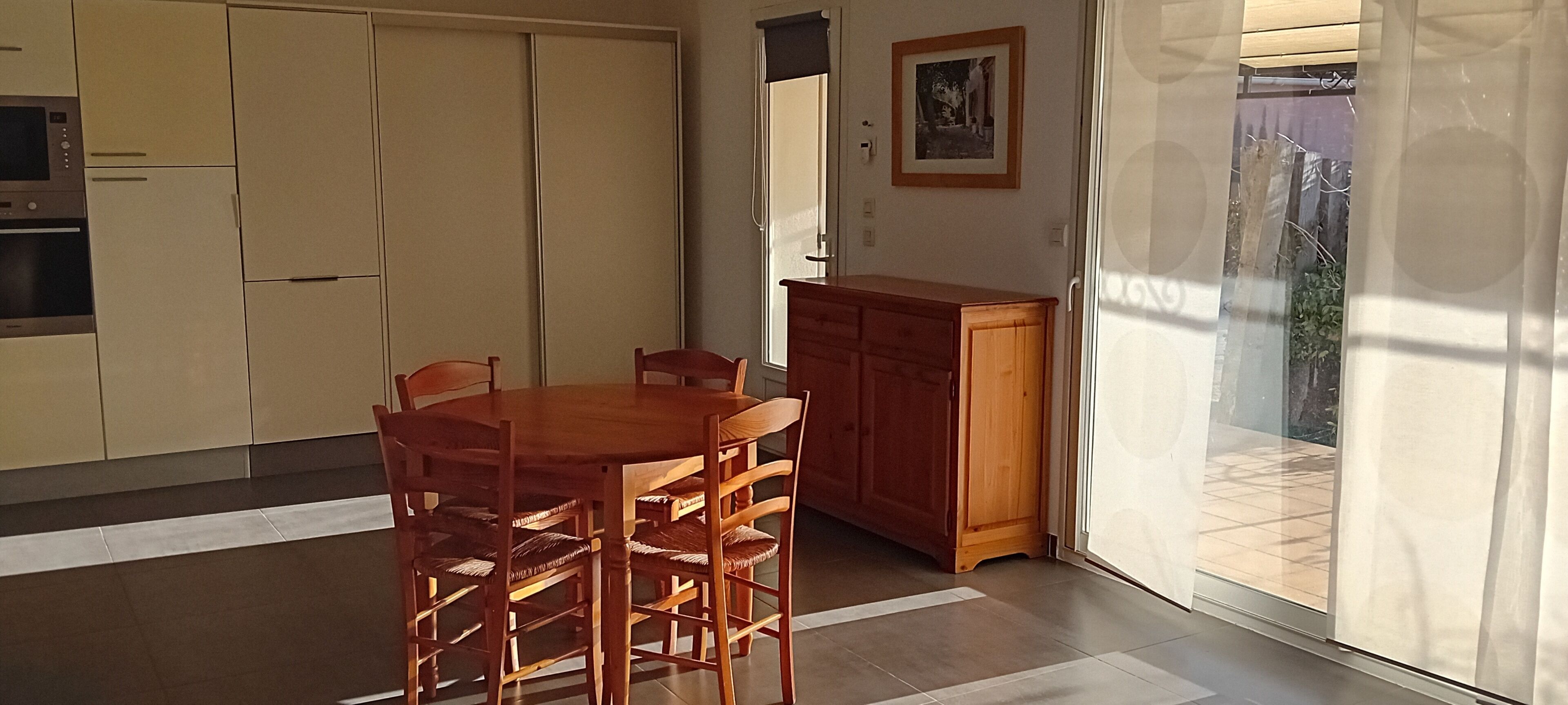 Un comedor con mesa y sillas de madera, un armario de madera y un ventanal corredero que da a un espacio exterior.