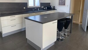 Een moderne keuken met een centraal eiland, barstoelen, een ingebouwde oven en een raam boven de spoelbak.