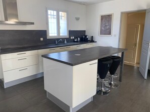 A modern kitchen with a central island, bar stools, a built-in oven, and a window above the sink. - Comfortable villa with pool in Provence (Mirabel-aux-Baronnies)