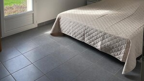 Een slaapkamer met een bed, een klein nachtkastje, een ingelijst kunstwerk aan de muur en een uitzicht op een groen landschap door een deur.