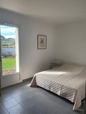 A bedroom with a bed, a small bedside table, a framed picture on the wall, and a view of a green landscape through a door. - Comfortable villa with pool in Provence (Mirabel-aux-Baronnies)