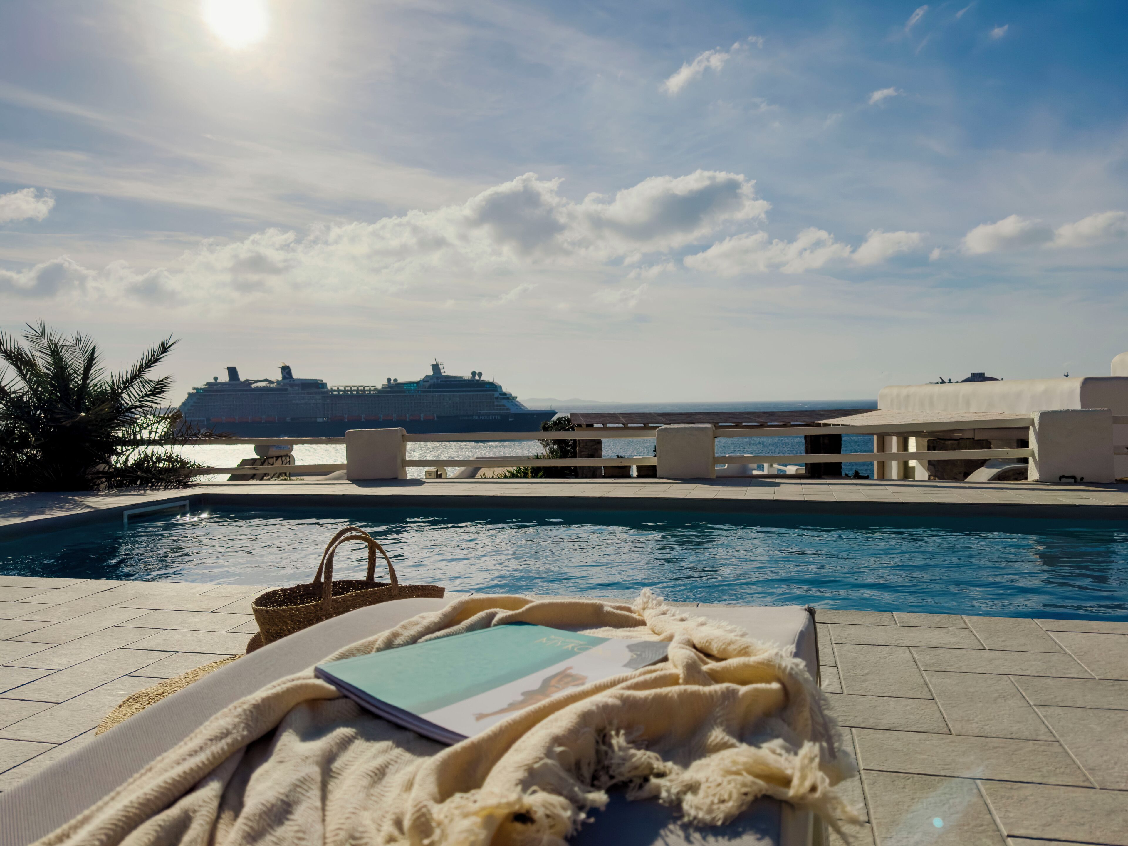 Un espace aménagé au bord de la piscine, avec un fauteuil de relaxation, un livre et une vue sur un navire de croisière au loin.