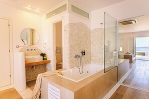 A modern bathroom with a large bathtub, a round mirror, and a stone-textured wall.