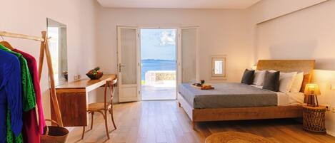 A bedroom with a bed, a desk, and a view of the sea.