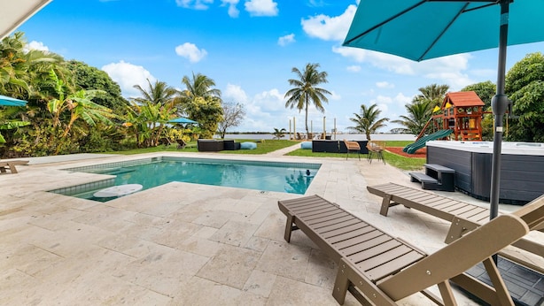 A pool area with lounge chairs, a hot tub, and a slide. - Waterfront Stunner! Heated Pool+Spa+Sauna+Firepit+ Playground! (West Palm Beach)