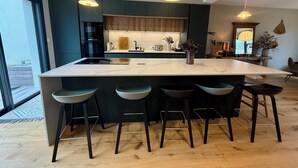 Une cuisine moderne dotée d’un grand îlot central, de meubles de rangement aux couleurs sombres et d’un éclairage suspendu.