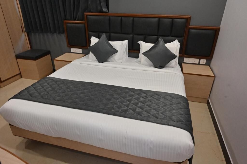 A neatly made bed with a black quilted bedspread and white linens, flanked by two nightstands with wooden sides and black cushioned headboards.