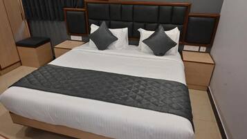A neatly made bed with a black quilted bedspread and white linens, flanked by two nightstands with wooden sides and black cushioned headboards.