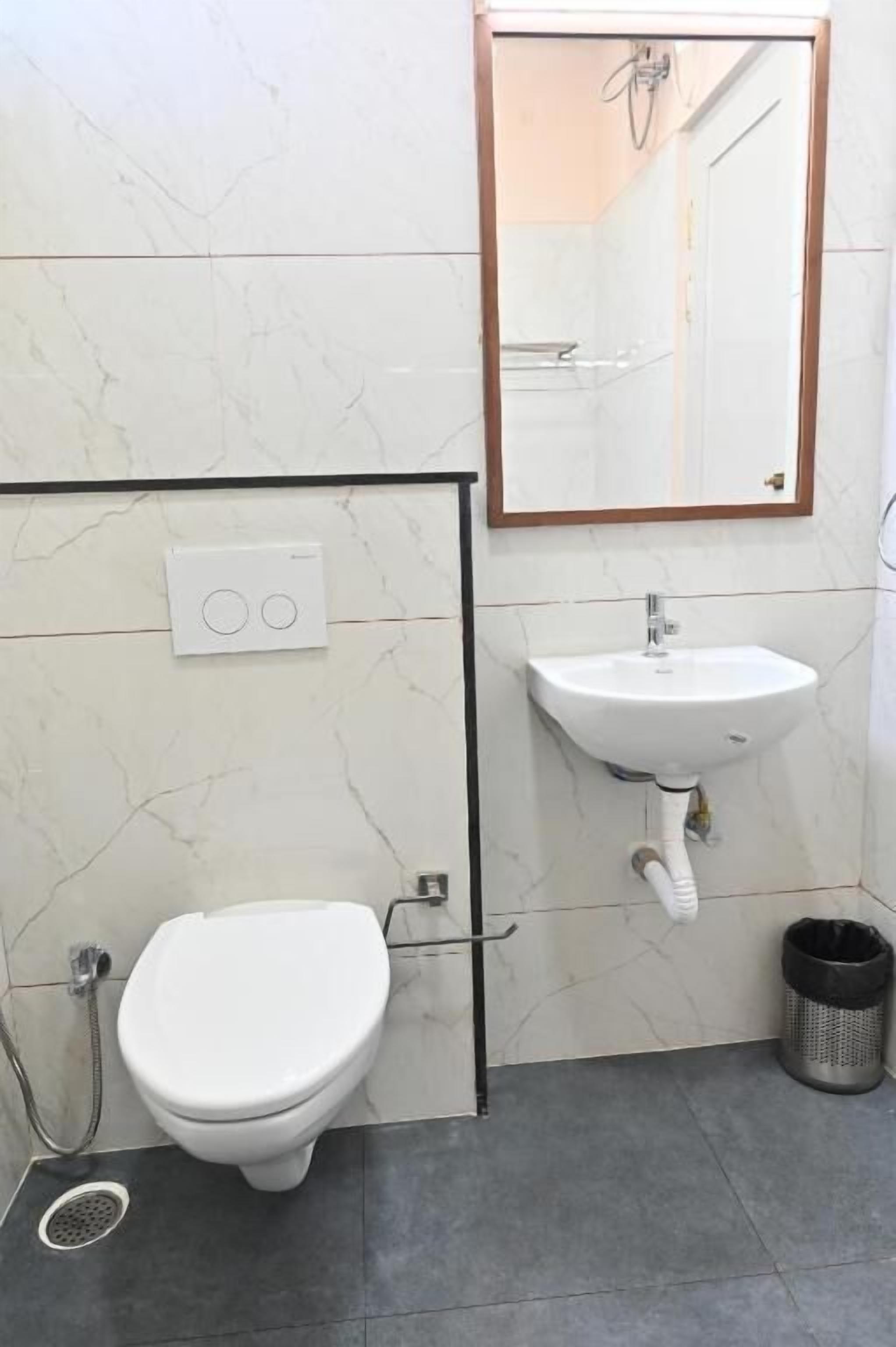 A bathroom with a toilet, sink, mirror, and a trash bin.