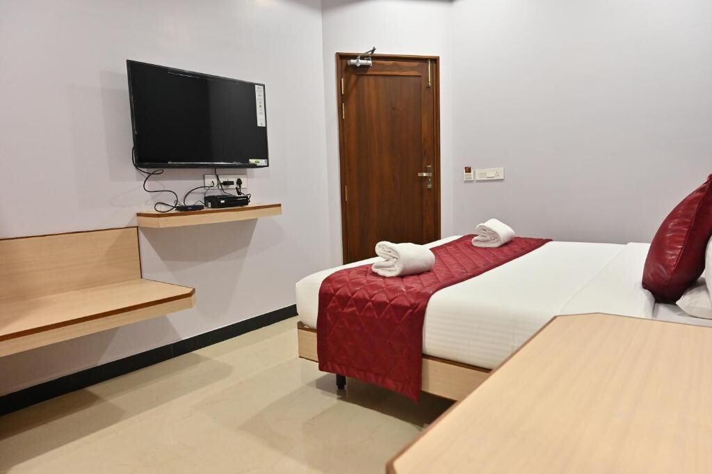 A hotel room with a bed, a TV mounted on the wall, a wooden nightstand, and a door.
