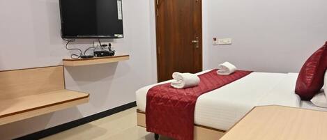Habitación de hotel con cama, televisor montado en la pared, mesita de noche de madera y una puerta.