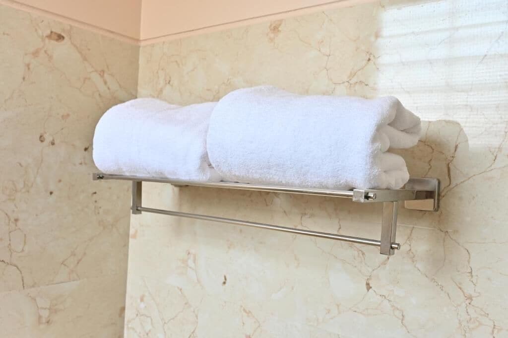 A bathroom with a marble wall and a towel rack holding two rolled towels.