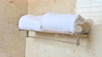 A bathroom with a marble wall and a towel rack holding two rolled towels.