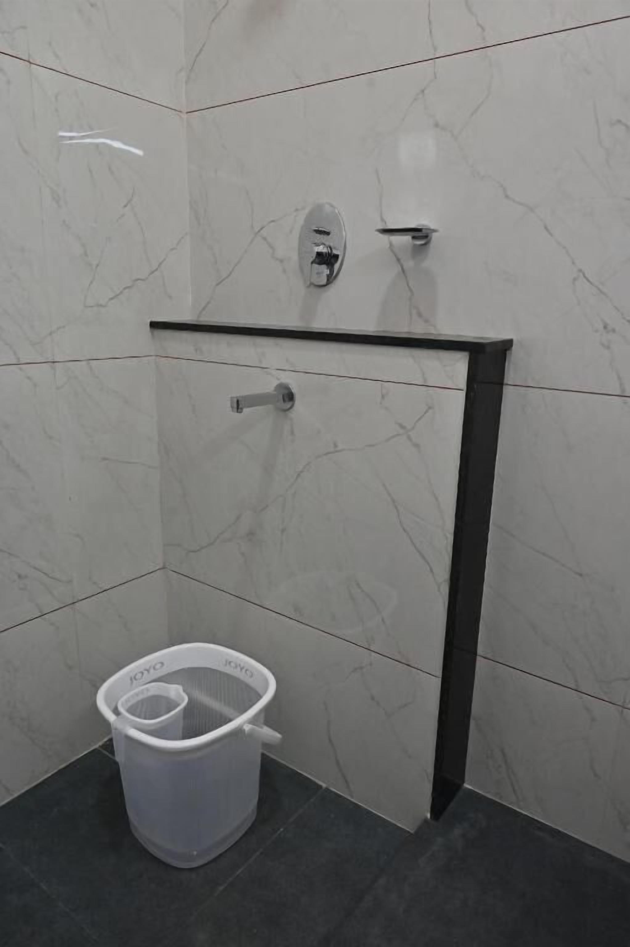 Ein Badezimmer mit Marmorwand, einem schwarzen Handtuchhalter und einem weißen Kunststoffkorb.