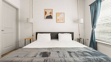 A modern hotel room with a large bed, two wall-mounted lamps, and abstract artwork.