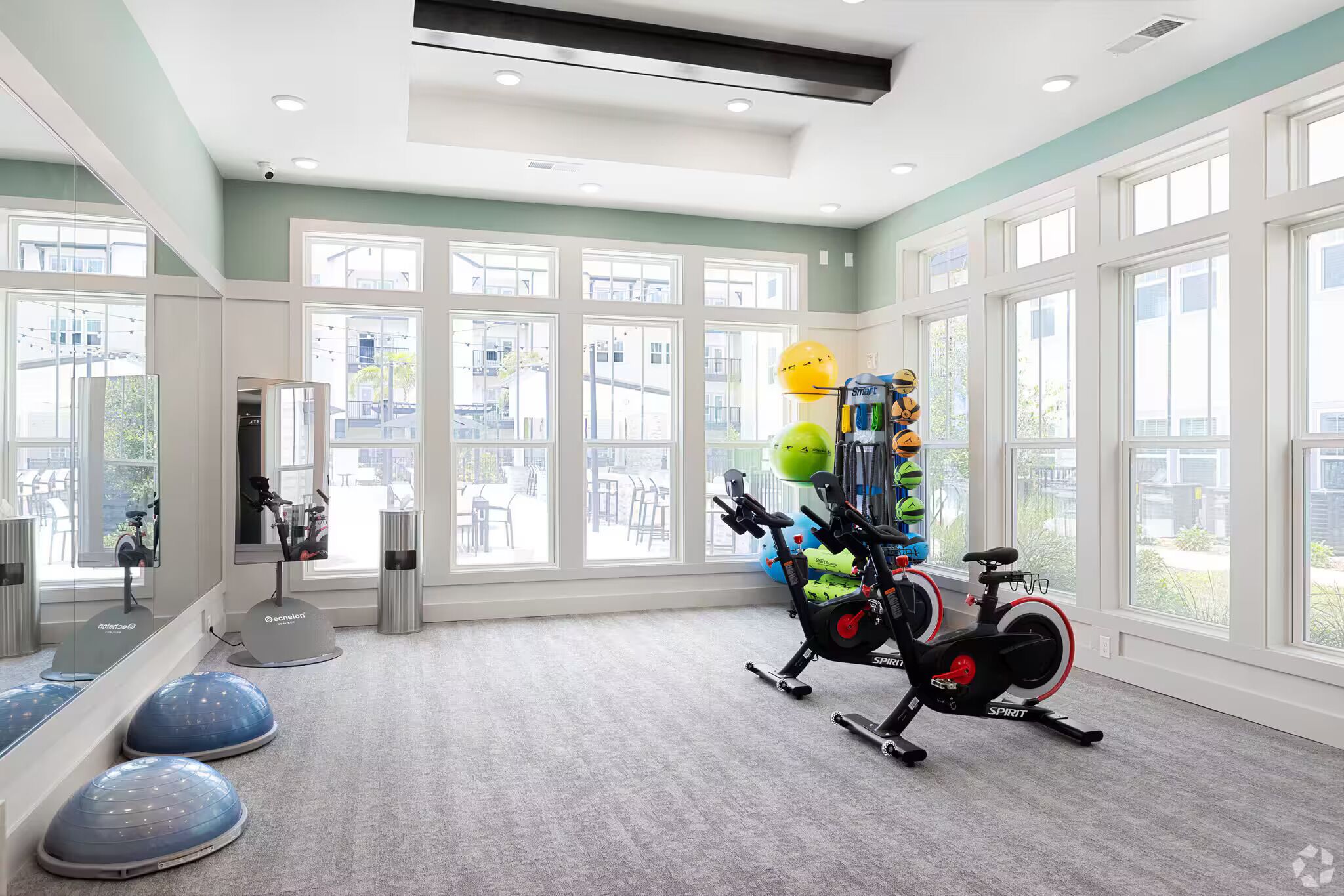 A spacious room with large windows, a stationary bike, and various exercise equipment.