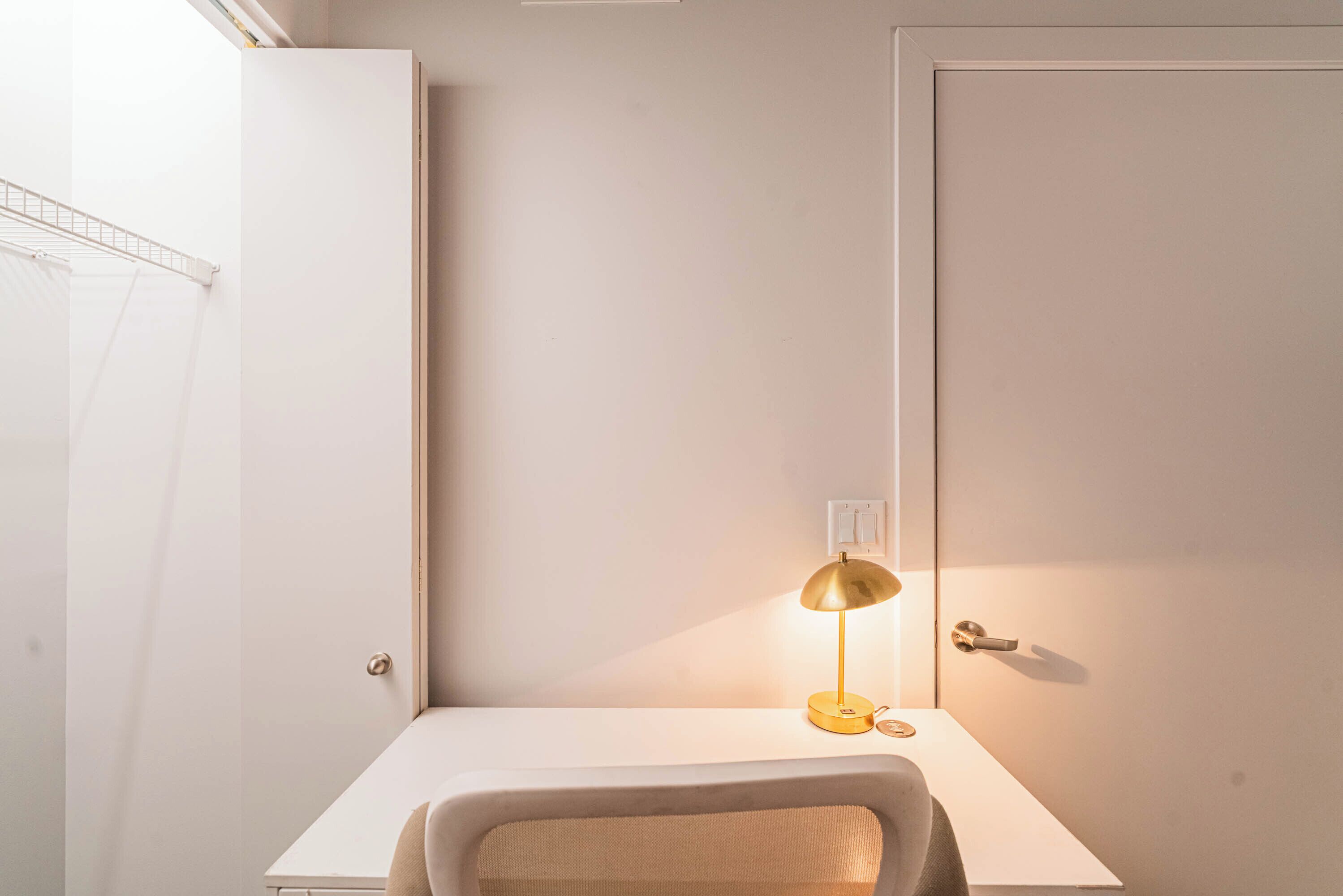 A minimalist room with a white desk, a gold lamp, and a chair.