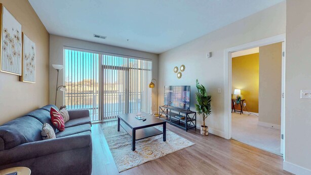 A modern living room with a sofa, coffee table, TV, and a large window with blinds. - Great Charming stay (Stamford)