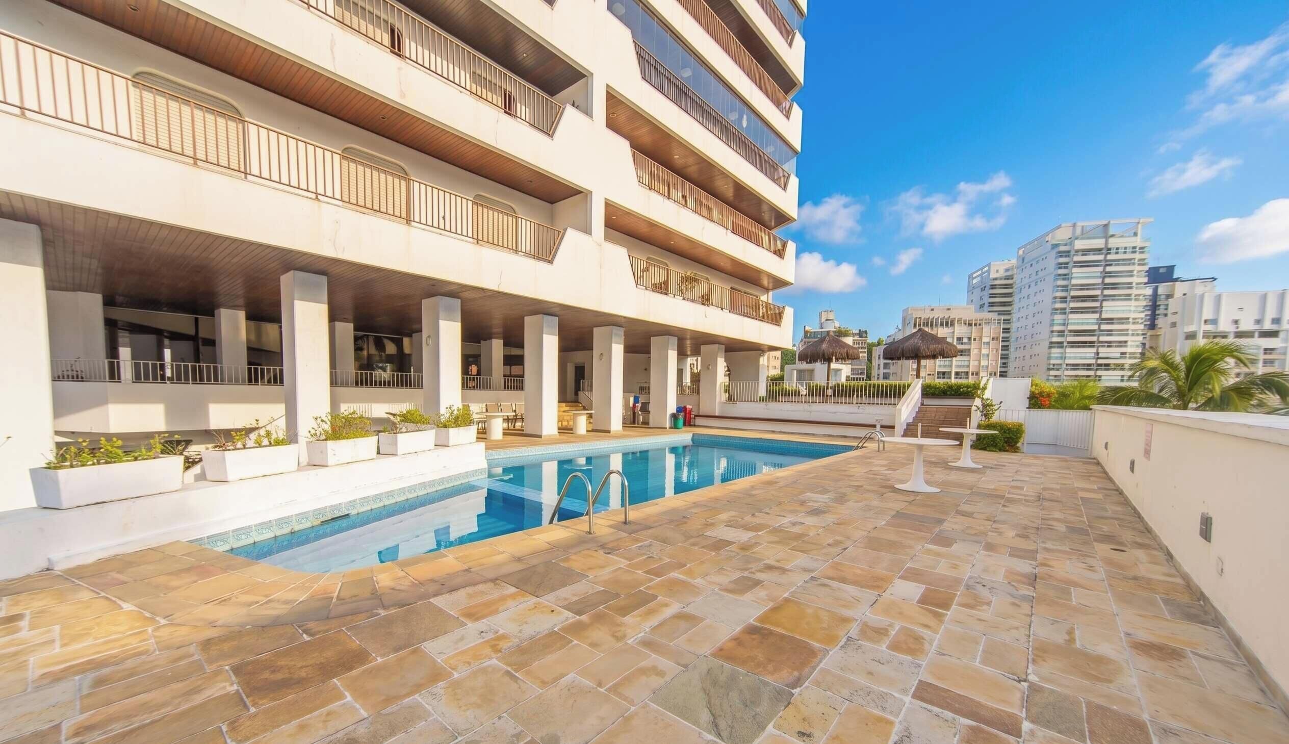 A multi-story hotel with a swimming pool, outdoor seating, and a view of surrounding buildings.