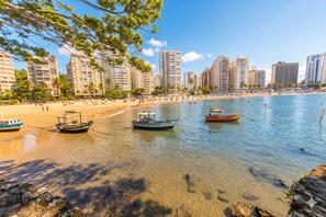 A beach with clear water, boats, and tall buildings in the background. - Apto no Guaruja com Piscina e Vista para o Mar (Guaruja)