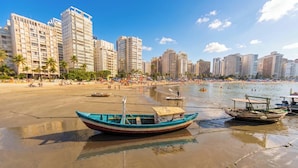 Een strand met boten, palmbomen en hoge gebouwen op de achtergrond.