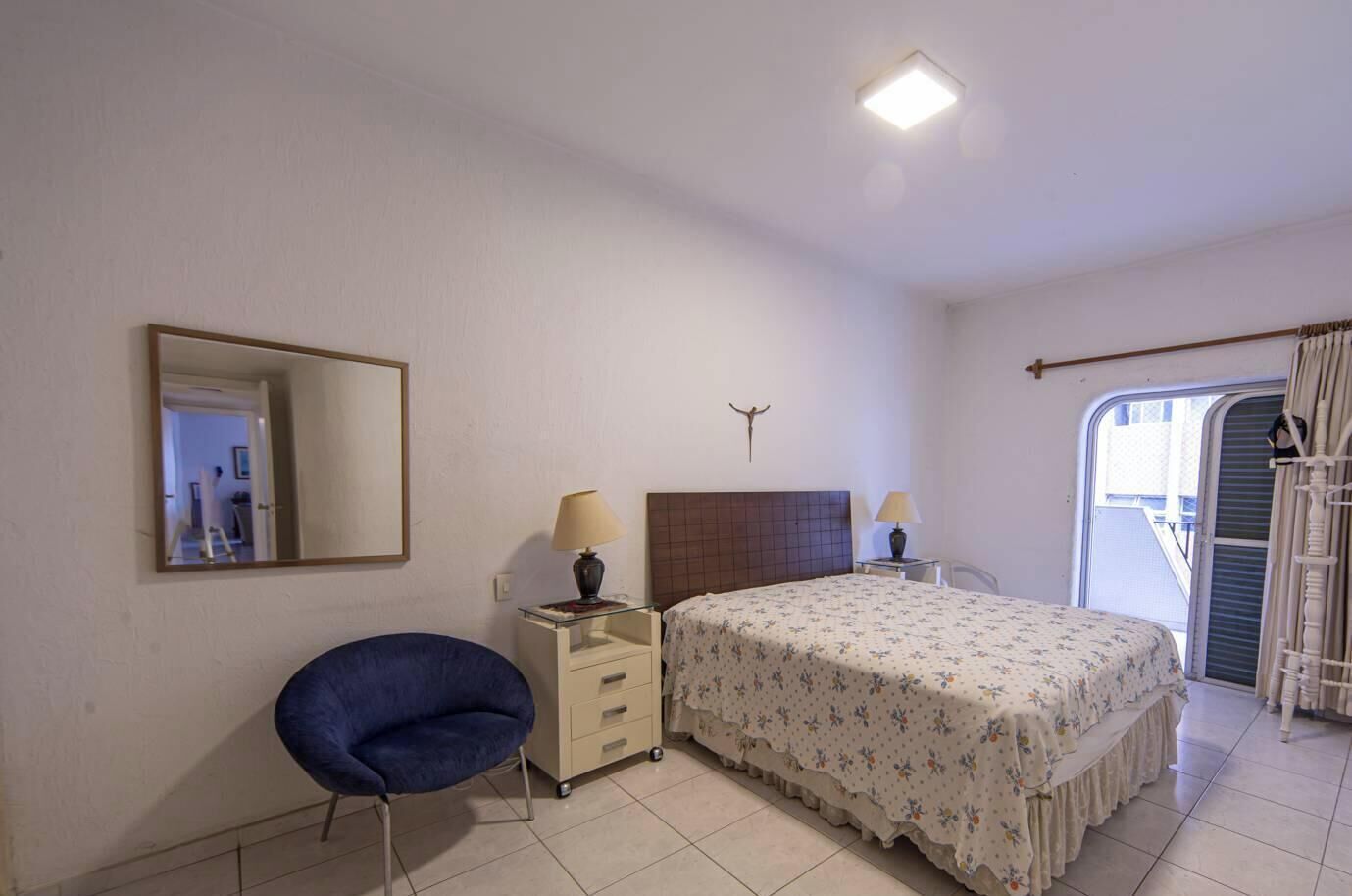 A bedroom with a bed, a chair, a nightstand, a mirror, and a window with curtains.