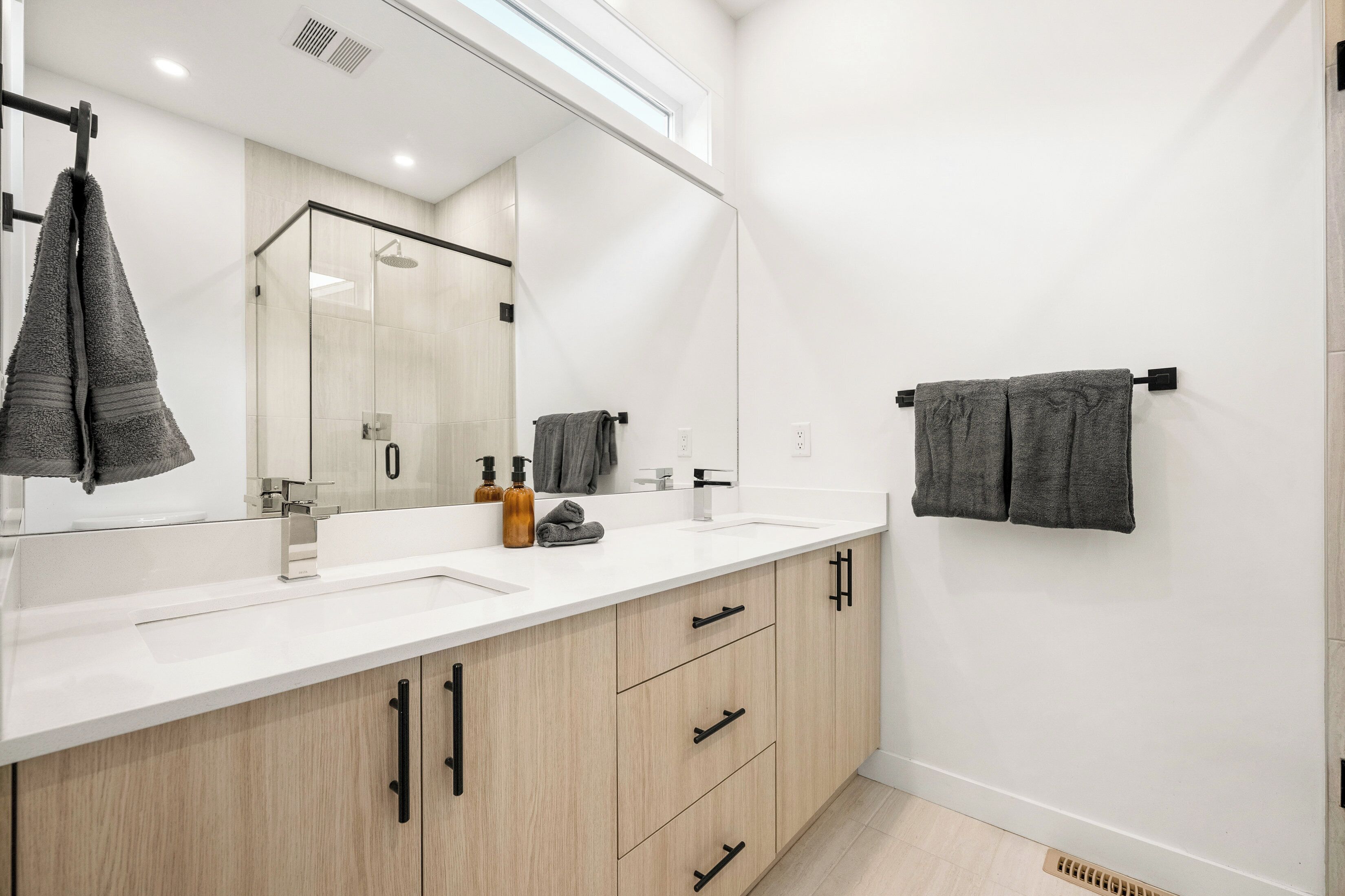 Une salle de bain moderne avec deux vasques, un grand miroir, des meubles en bois et un porte-serviettes.