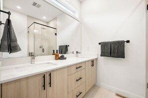 A modern bathroom with two sinks, a large mirror, wooden cabinets, and a towel rack. - Three Sisters Villas | 9BD 6BA | 7 mins DT |20 ppl (Calgary)