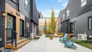 Un patio con un camino pavimentado, mobiliario exterior y un árbol pequeño.