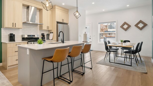 Una cocina moderna con una isla central, taburetes de bar y un comedor con mesa y sillas.