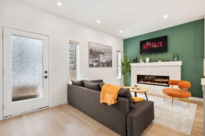 A modern living room with a grey sofa, a fireplace, a TV mounted on the wall, and a green accent wall. - Three Sisters Villas | 9BD 6BA | 7 mins DT |20 ppl (Calgary)