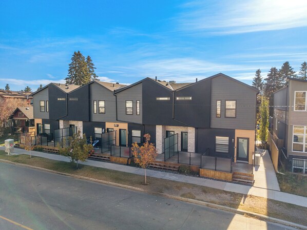 A modern townhouse with a flat roof, large windows, and a visible address number. - Three Sisters Villas | 9BD 6BA | 7 mins DT |20 ppl (Calgary)