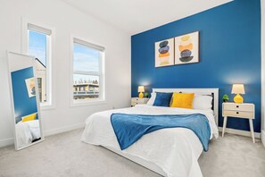 A modern bedroom with a large bed, two bedside tables with lamps, a mirror, and a view of the outside. - Three Sisters Villas | 9BD 6BA | 7 mins DT |20 ppl (Calgary)