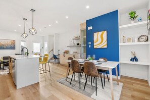 A modern kitchen with a central island, a dining area with chairs, and a blue accent wall. - Three Sisters Villas | 9BD 6BA | 7 mins DT |20 ppl (Calgary)