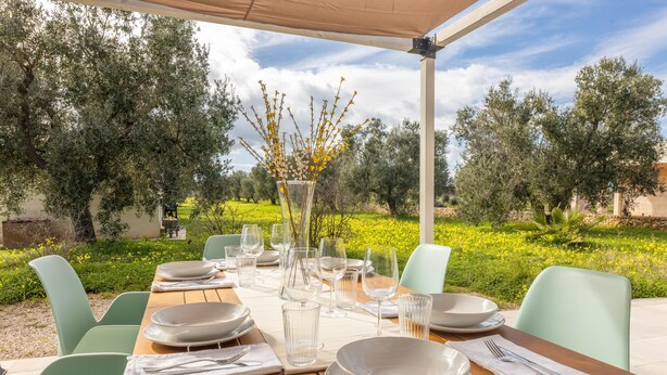 An outdoor dining area with a wooden table set for six, surrounded by light green chairs. - Casale Calia - Carovigno (Carovigno)