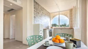 A modern kitchen with a dining area, featuring a large window, a decorative backsplash, and a table set with a bowl of oranges and two mugs. - Casale Calia - Carovigno (Carovigno)