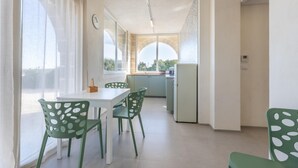 A modern kitchen with a dining area, featuring a white table, green chairs, and a view through an arched window. - Casale Calia - Carovigno (Carovigno)
