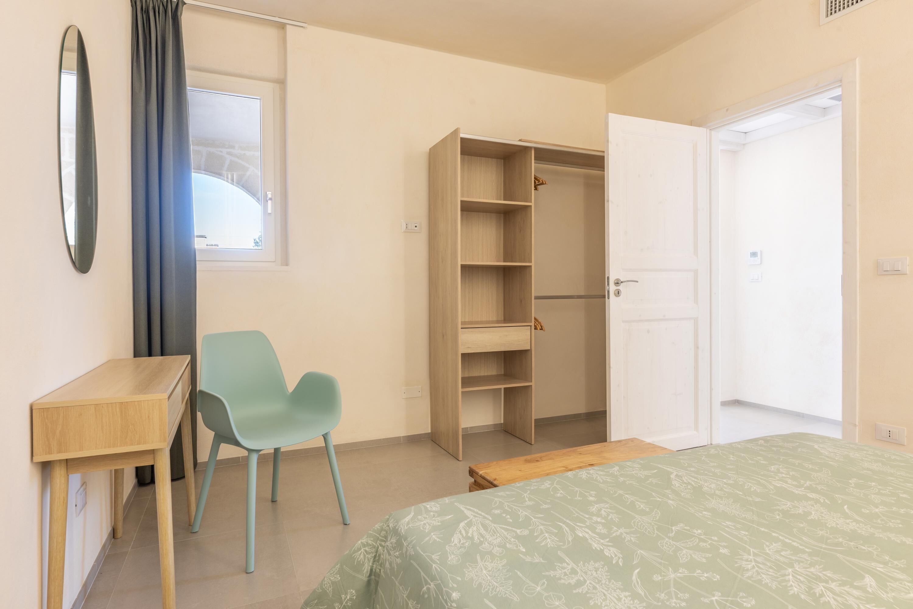 A bedroom with a bed, a desk, a chair, a wardrobe, and a window.