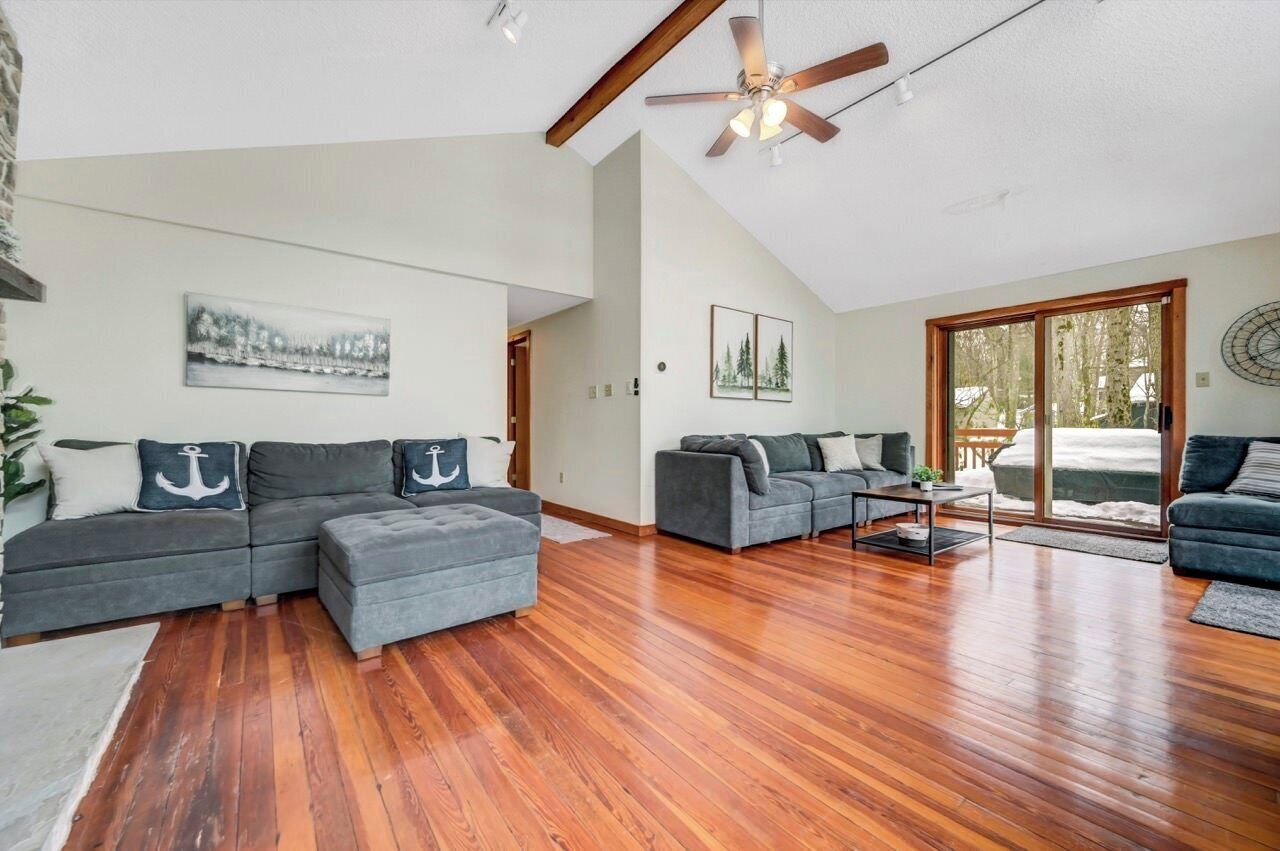 A spacious living room with a wooden floor, a ceiling fan, and two grey sofas with anchor pillows.