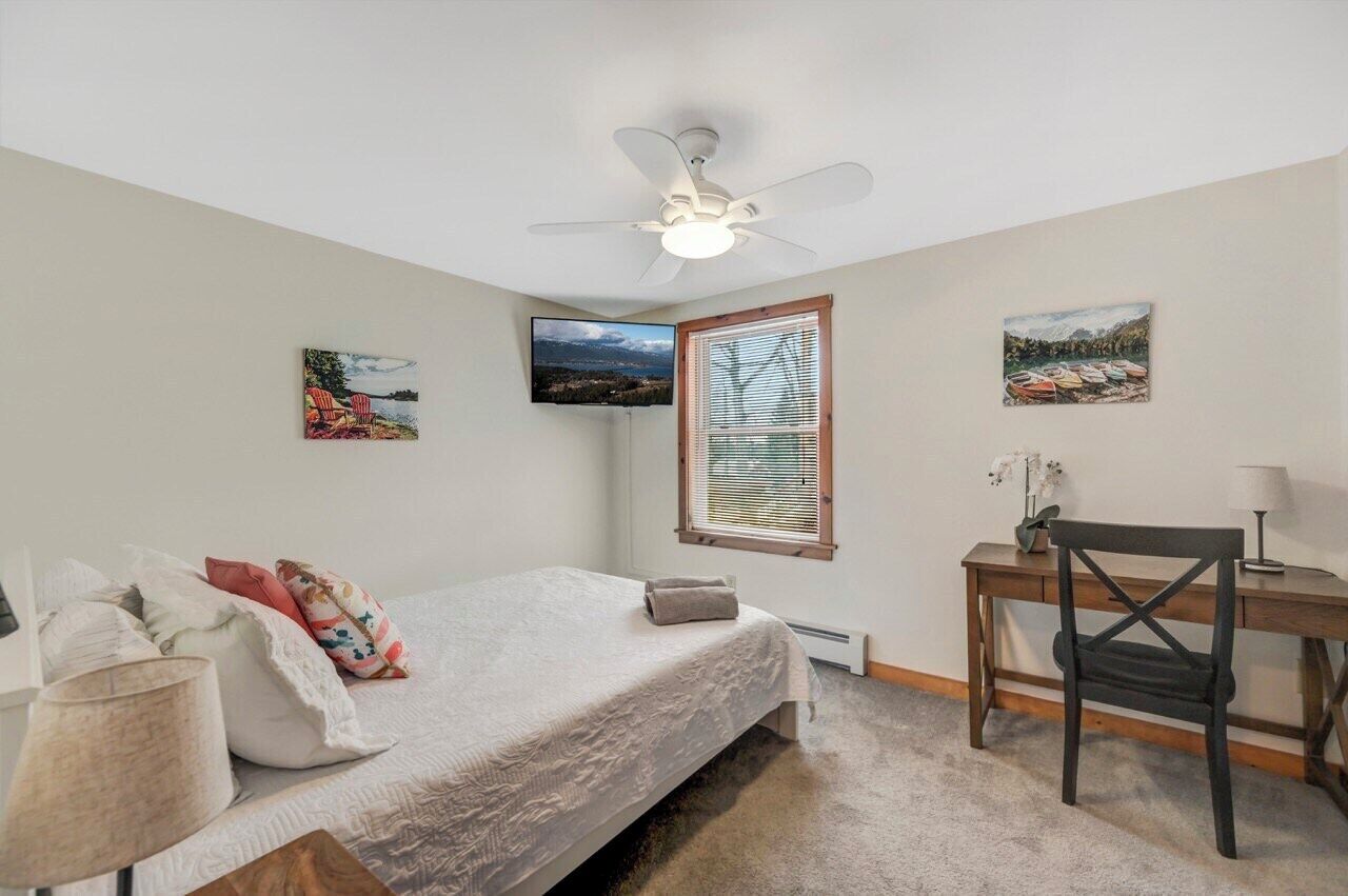 Un dormitorio con cama, escritorio, silla, ventilador de techo y obras de arte en la pared.